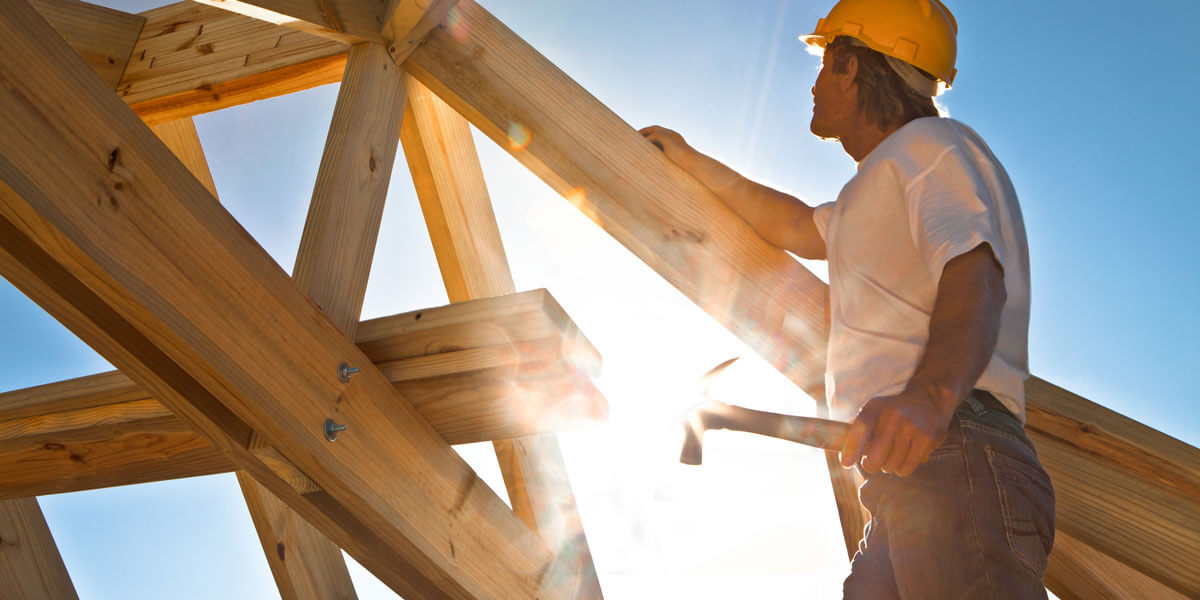 Roofer holding hammer, sun in background.