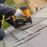 roofer using nail gun to install shingles